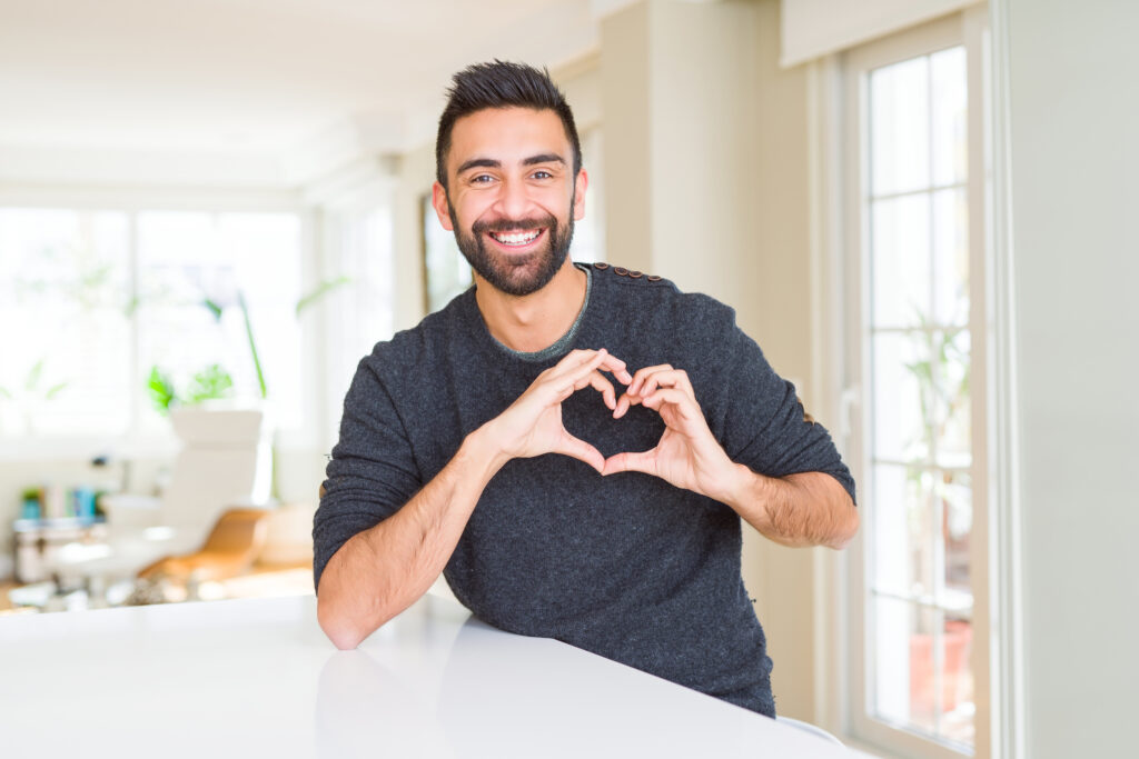 Man smiling and using hands to create a heart on his chest
