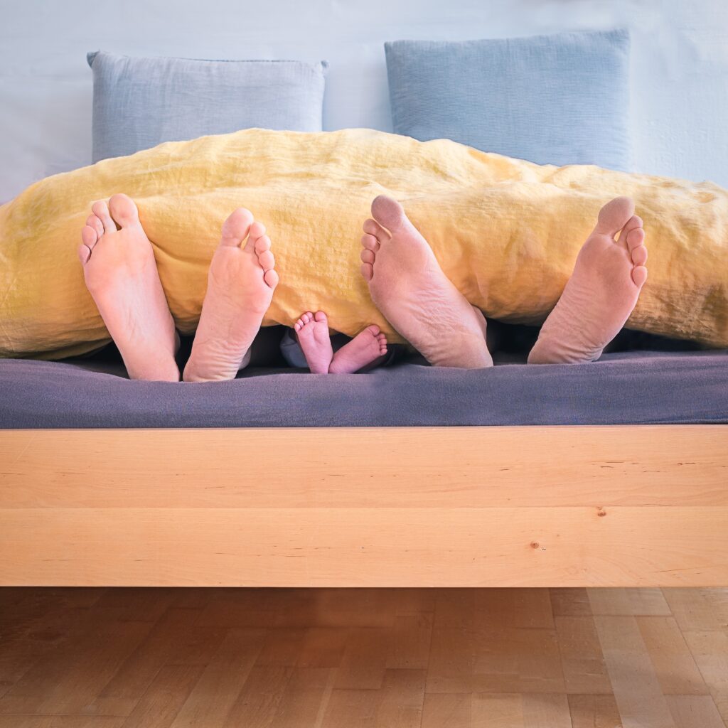 Parents and kids sticking feet out of covers in the same bed